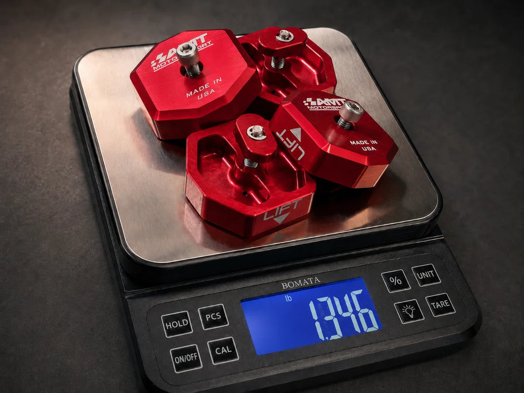 Four red AMT Switchblade jacking pucks arranged on a digital scale reading 1.346 lb, showing the complete aluminum lift-pad set