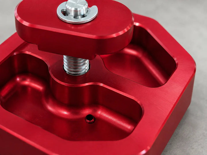 Close view of the small drainage opening inside a red AMT Switchblade jacking puck, alongside the recessed machined body pockets