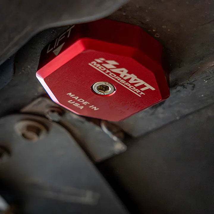 Red AMT Switchblade jacking puck secured at an underbody lift point, with the center screw seated in the marked aluminum contact face