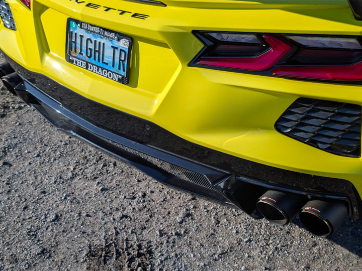Carbon fiber exhaust tips fitted under the rear fascia of a yellow C8 Corvette, photographed from behind the car