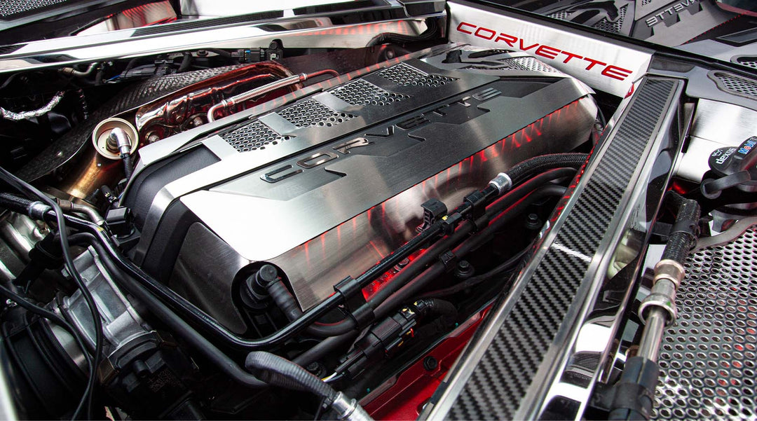 ACC 883026 carbon-fiber-topped rear crossmember cover with brushed stainless trim beside a C8 Corvette Coupe engine shroud; other dress-up parts are separate