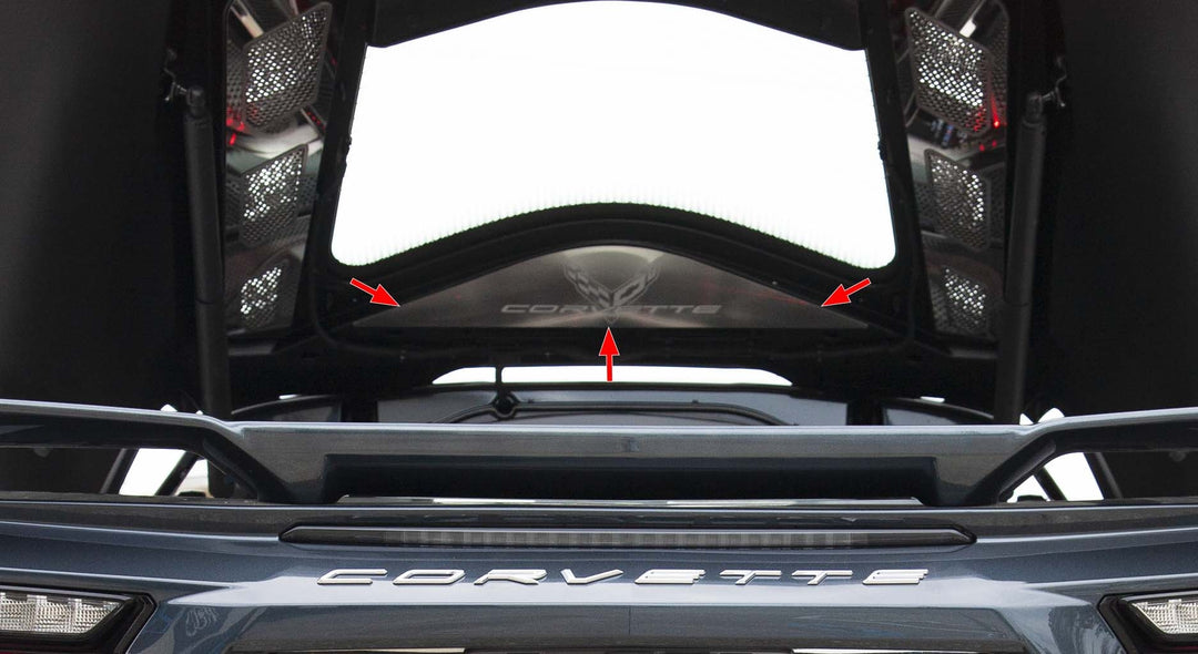 Lower-angle view of the brushed stainless vanity plate beneath an open C8 Corvette Coupe rear hatch, with arrows marking the plate