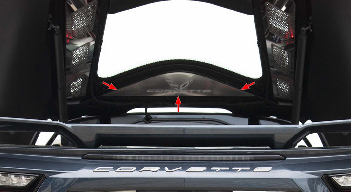 Lower-angle view of the brushed stainless vanity plate beneath an open C8 Corvette Coupe rear hatch, with arrows marking the plate