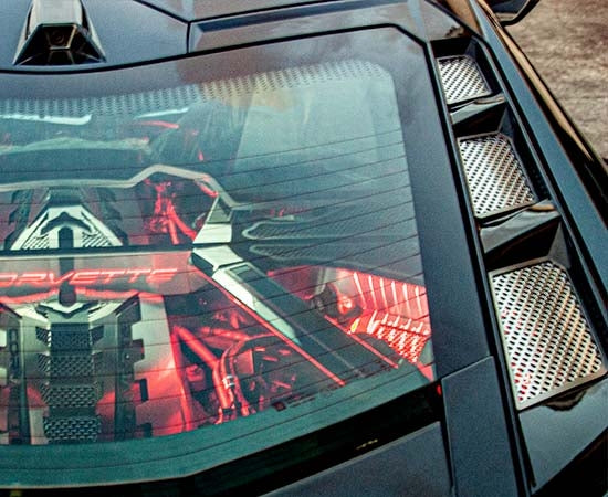 Polished perforated rear vent inserts beside the C8 Corvette Coupe rear window, with separate engine accessories in the background
