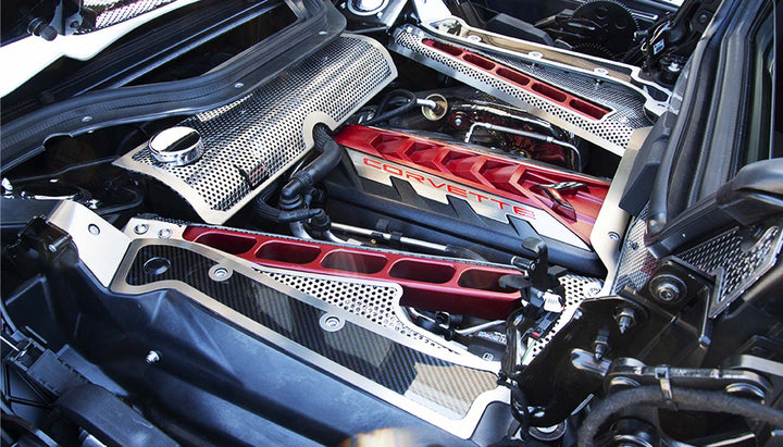 Carbon fiber frame-rail covers with brushed stainless trim on both sides of a C8 convertible engine bay