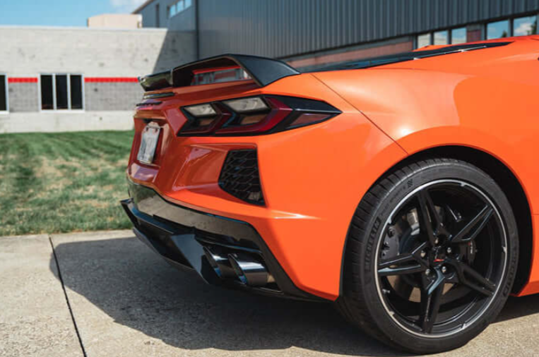 Polished CORSA quad exhaust tips in the rear diffuser of an orange C8 Corvette Stingray, three-quarter rear view